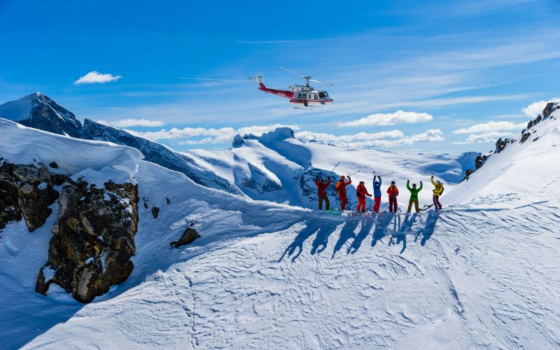 helicopter-skiing-group-standing-on-a-slope-waving-at-helicopter-min