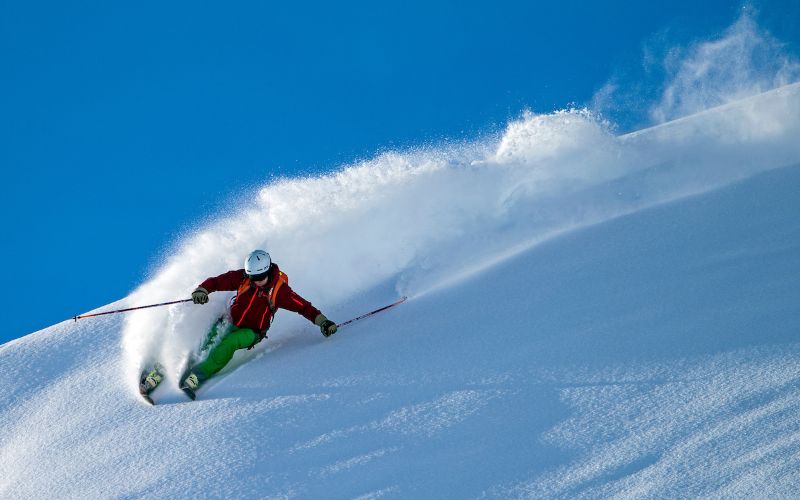 helicopter-skiing-skier-carving-through-deep-powder-min