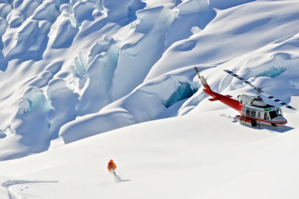 heli-skiing-canada-mountain-range-with-helicopter-in-foreground-min