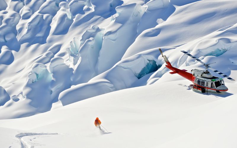 heli-skiing-canada-lone-skier-next-to-helicopter-min