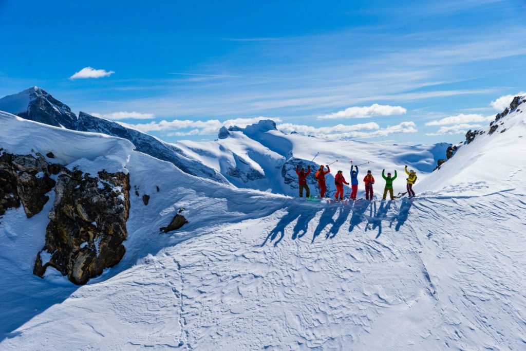 heli-skiing-canada-multiple-skiers-on-peak-min